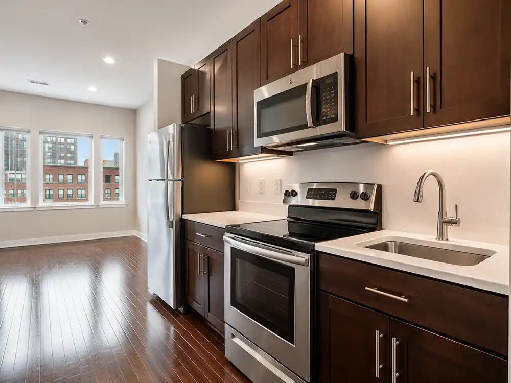 Modern kitchen with dark wood cabinets, stainless steel appliances, white countertops, and hardwood floors overlooking city buildings.